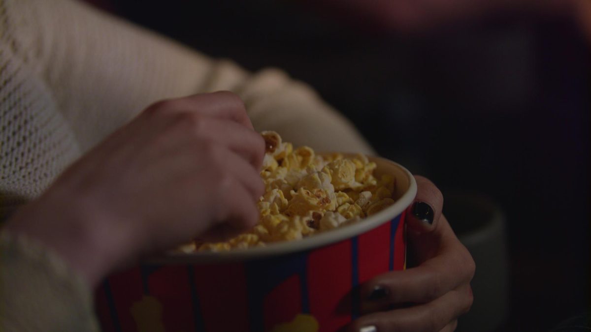 Hand in a popcorn bucket in a movie theatre via Storyblocks.
