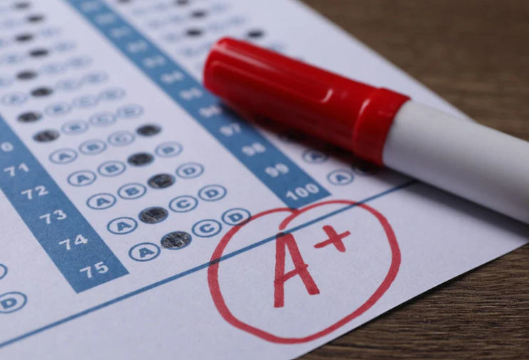School Grade. Answer Sheet with Red Letter a, plus Symbol and Marker on Wooden Table, Closeup by Africa images via Canva
